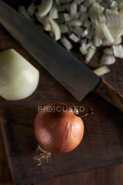 De arriba trozos de cebolla cortada colocados cerca de cuchillo sobre mesa de madera en cocina - foto de stock