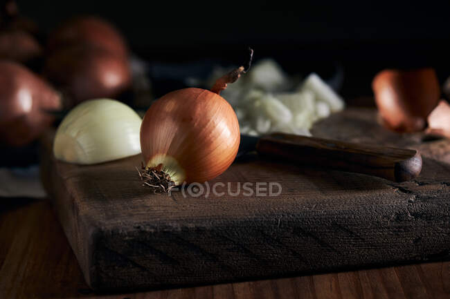 Сельский чаша с кусочками вырезанного лука помещен рядом с ножом на деревянный стол на кухне — стоковое фото