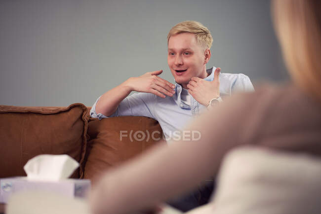 Занепокоєний чоловік сидить на дивані і виступає під час сеансу психотерапії з психологом — стокове фото
