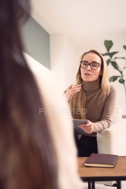 Consulente femminile seduta in poltrona e che dà consigli a clienti irriconoscibili durante l'appuntamento in psicoterapia — Foto stock