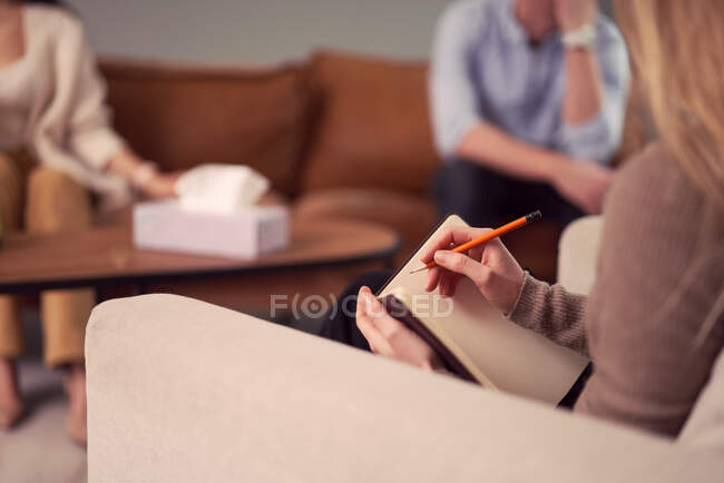 Psicólogo feminino irreconhecível falando notas no caderno durante sessão de terapia com casal no escritório — Fotografia de Stock