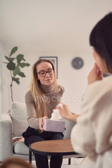 Consulente femminile ascoltando cliente anonimo mentre aiuta durante la sessione di terapia mentale e dando tessuti — Foto stock
