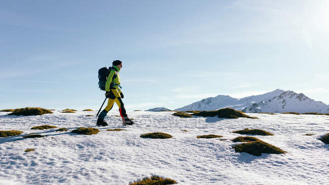 Вид збоку на невизначений альпініст, що йде на схил снігу, покритий скелястим гірським хребтом у сонячну погоду — стокове фото