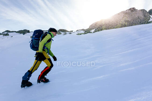 Side view of climber walking on slope of snow covered rocky mountain range in sunny weather — Stock Photo