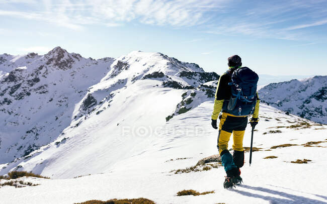 Вид ззаду на невідомий альпініст, що йде на схилі снігу, покритий скелястим гірським хребтом у сонячну погоду — стокове фото