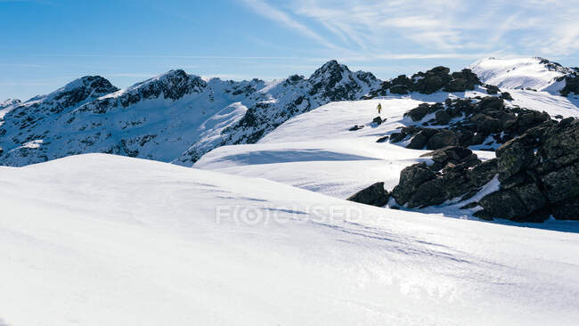 Distant unrecognizable climber walking on slope of snow covered rocky mountain range in sunny weather — Stock Photo