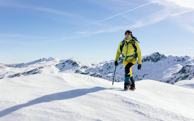 Альпинист во внешней части прогулки по склону покрытой снегом скалистой горной цепи в солнечную погоду — стоковое фото