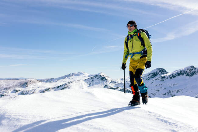 Male climber in outwear walking on slope of snow covered rocky mountain range in sunny weather — Stock Photo