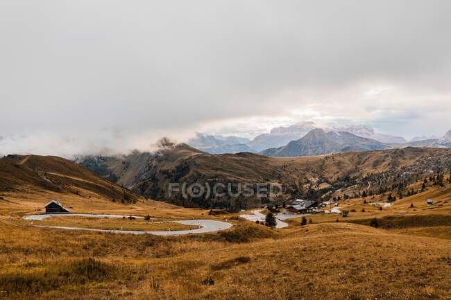 Paysage pittoresque avec pic rocheux escarpé rugueux et collines couvertes d'herbe jaune sous les nuages dans la chaîne de montagnes Dolomites en Italie — Photo de stock