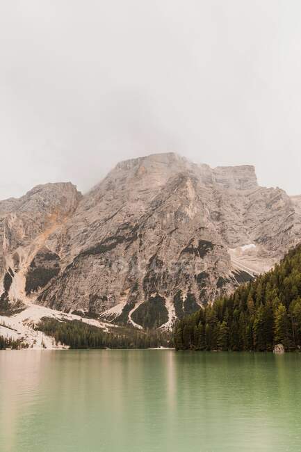 Удивительный вид горного хребта Доломиты с зеленой водой озера, отражающей грубые скалистые склоны, покрытые туманом и облаками в Италии — стоковое фото