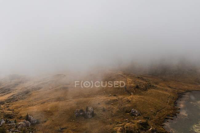 Dall'alto paesaggio panoramico di laghetto circondato da colline ricoperte di nebbia e nuvole nella catena montuosa dolomitica in Italia — Foto stock