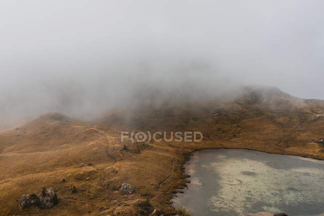 З - над мальовничого краєвиду маленького озера, оточеного пагорбами, вкритими туманом і хмарами в гірському хребті Доломіти в Італії. — стокове фото