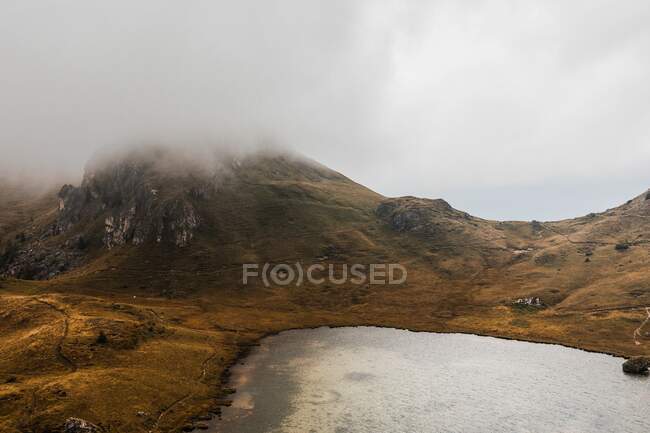 З - над мальовничого краєвиду маленького озера, оточеного пагорбами, вкритими туманом і хмарами в гірському хребті Доломіти в Італії. — стокове фото