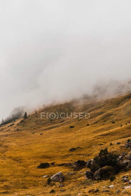 Paesaggio pittoresco con ripida cima rocciosa e colline coperte di erba gialla sotto le nuvole nella catena montuosa dolomitica in Italia — Foto stock