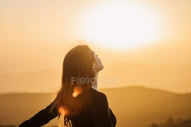 Vista lateral da fêmea feliz em pé com os olhos fechados na colina e desfrutando de liberdade enquanto admira paisagens montanhosas ao pôr do sol — Fotografia de Stock