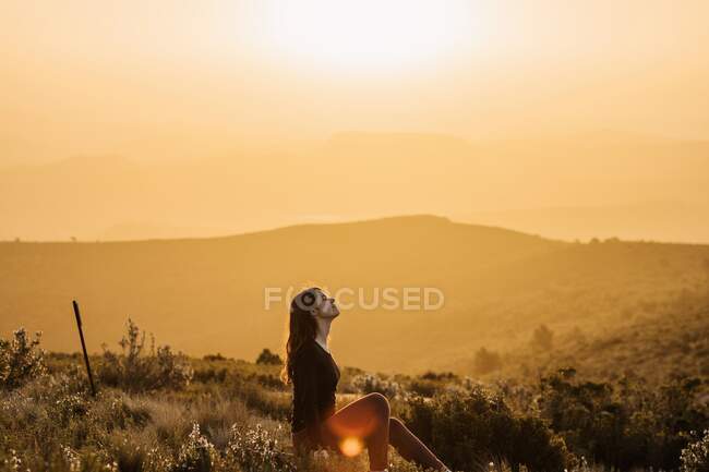 Seitenansicht einer friedlichen Reisenden, die mit geschlossenen Augen auf einem Hügel sitzt und die Natur im Hochland bei Sonnenuntergang genießt — Stockfoto