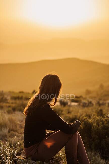 Vue latérale d'une voyageuse paisible assise sur une colline les yeux fermés et profitant de la nature dans les hautes terres au coucher du soleil — Photo de stock