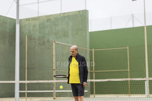 Esportista sênior saltando bola na raquete enquanto se prepara para o jogo de tênis no campo — Fotografia de Stock