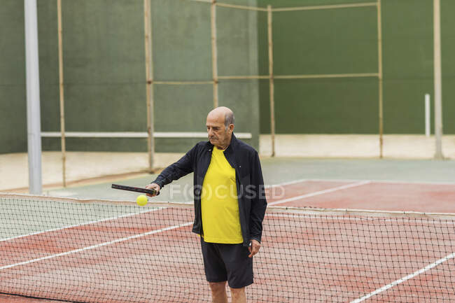 Старший спортсмен прыгает мяч на ракетку во время подготовки к теннисному матчу на корте — стоковое фото