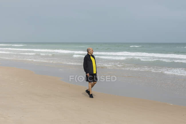 Sportif âgé marchant sur la plage près de la mer agitant pendant l'entraînement de remise en forme en été — Photo de stock