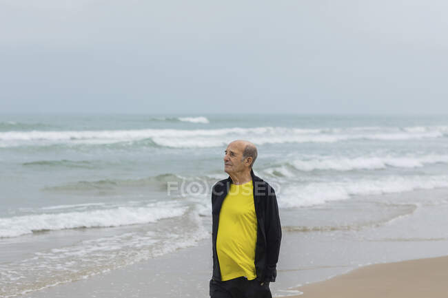 Elderly sportsman walking on beach near waving sea during fitness workout in summer — Stock Photo