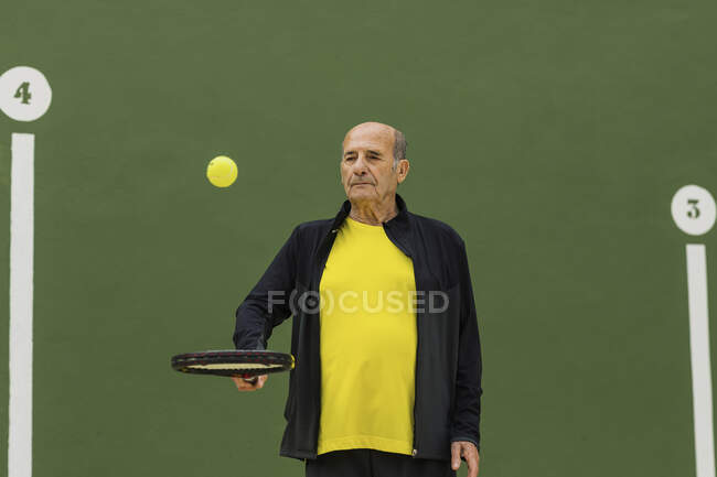 Esportista sênior saltando bola na raquete enquanto se prepara para o jogo de tênis no campo — Fotografia de Stock