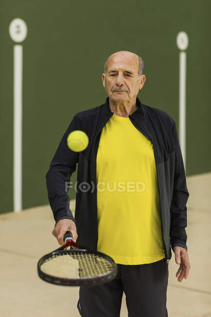 Sportivo senior che rimbalza palla sulla racchetta mentre si prepara per la partita di tennis in campo — Foto stock