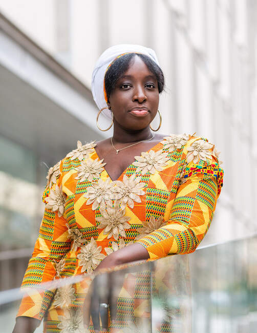 Young African female in bright wear with floral ornament looking at camera near glass fence in city — Stock Photo