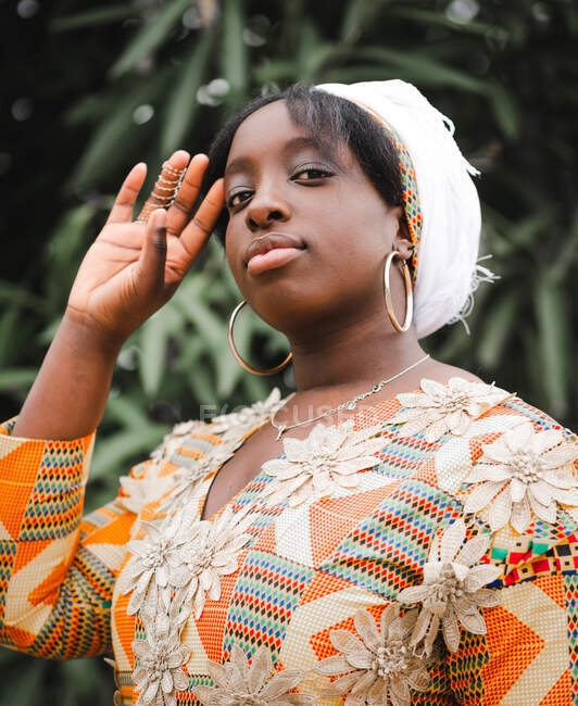 Молодая африканская женщина в платке смотрит в камеру на растение летом — стоковое фото