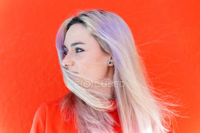 Young contemplative friendly female in earring with dyed hair looking down on bright background — Stock Photo