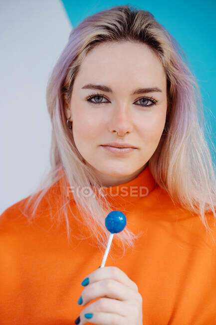 Charming young female in bright clothes with blond hair and lolly looking at camera in sunlight — Stock Photo