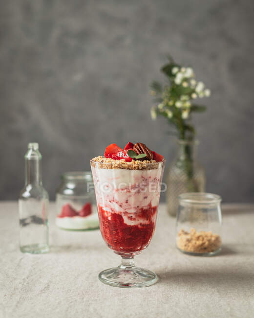 Стакан сладких вкусных ягод и вкусное мороженое, украшенное орехами и клубникой подается на столе возле стеклянных банок — стоковое фото