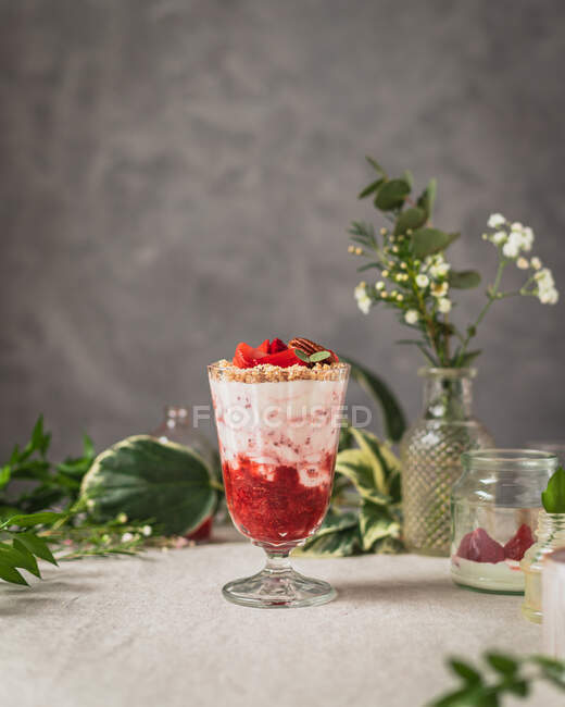 Стакан сладких вкусных ягод и вкусное мороженое, украшенное орехами и клубникой подается на столе возле стеклянных банок — стоковое фото