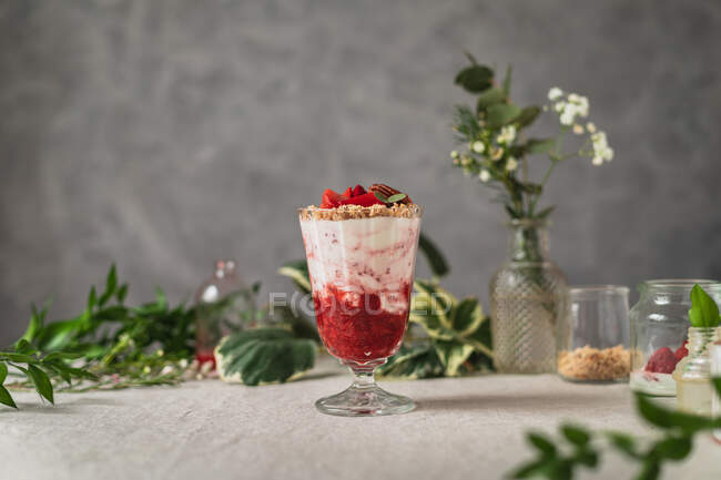 Copo de bagas saborosas doces e sorvete gostoso decorado com nozes e morangos servidos na mesa perto de frascos de vidro — Fotografia de Stock