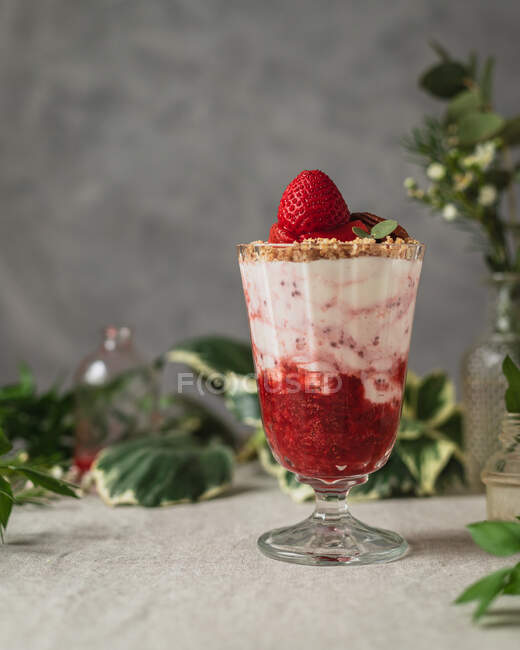 Verre de baies sucrées savoureuses et crème glacée délicieuse garnie de noix et de fraises servies sur la table près de bocaux en verre — Photo de stock