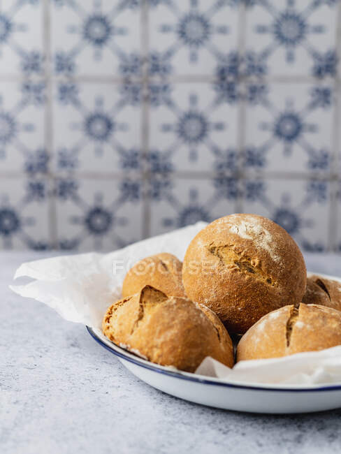 Appetizing freshly baked bread buns heaped on baking paper on plate and served on kitchen table — Stock Photo