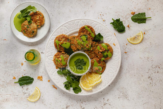Вкусные аппетитные травяные оладьи, украшенные зеленым соусом петрушки и ломтиками лимона на белом столе — стоковое фото