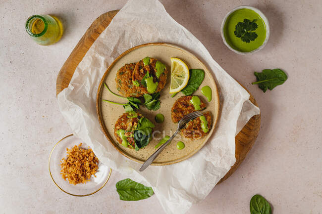 Top view composition of appetizing herbal fritters with green sauce and lemon slice served on wooden board and craft paper — Stock Photo