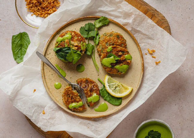 Composición vista superior de apetitosos buñuelos de hierbas con salsa verde y rodaja de limón servidos en tablero de madera y papel artesanal - foto de stock