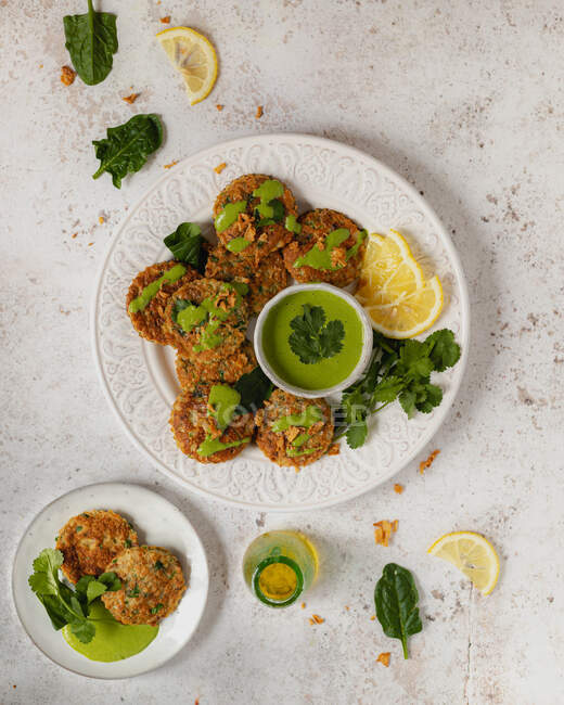 Vista superior deliciosos buñuelos de hierbas apetitosos adornados con perejil salsa verde saludable y rodajas de limón en la mesa blanca - foto de stock
