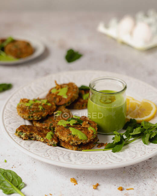 Yummy appetizing herbal fritters garnished with healthy green sauce parsley and lemon slices on white table — Stock Photo