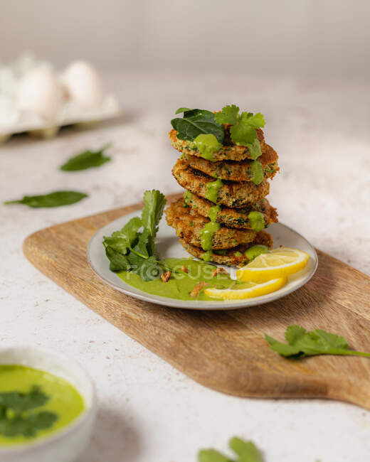 Frische leckere Kräuterfrikadellen gestapelt auf Teller und dekoriert mit grüner Sauce und Zitronenscheibe serviert auf Holzschneidebrett — Stockfoto