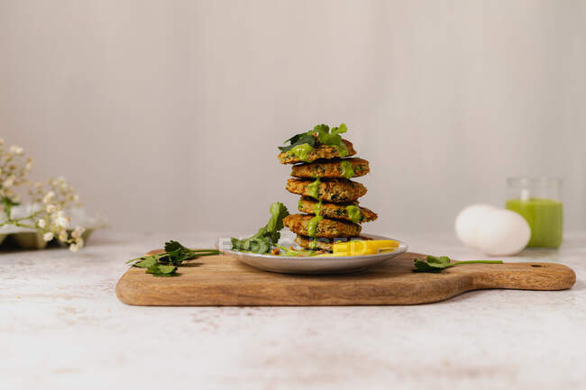 Fresh tasty herbal fritters stacked on plate and decorated with green sauce and lemon slice served on wooden cutting board — Stock Photo