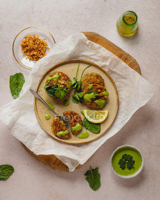Vista dall'alto composizione di appetitose frittelle alle erbe con salsa verde e fetta di limone servite su tavola di legno e carta artigianale — Foto stock