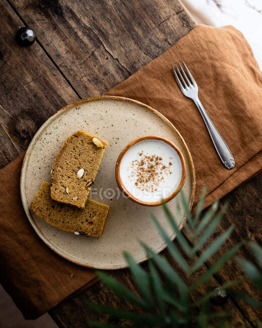 Верхний вид композиции ломтиков вкусного свежего цельнозернового хлеба подается на тарелке с чашкой свежего молока — стоковое фото