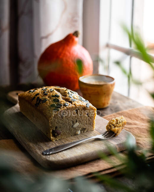 Through houseplant leaves yummy freshly baked pumpkin bread with wholesome grains placed on wooden cutting board in light kitchen — Stock Photo