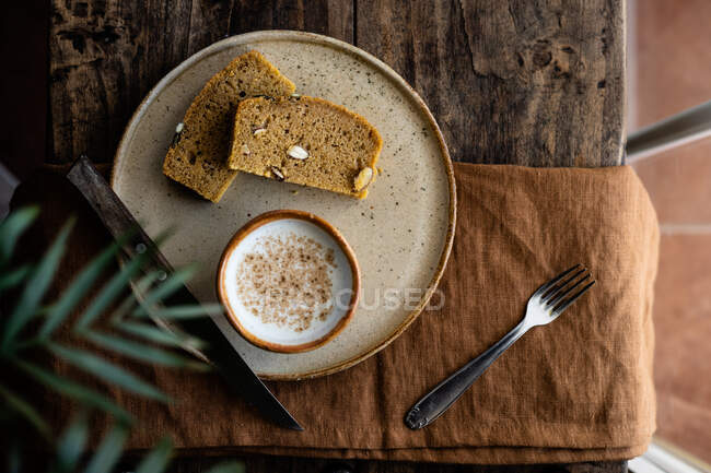 Верхний вид композиции ломтиков вкусного свежего цельнозернового хлеба подается на тарелке с чашкой свежего молока — стоковое фото