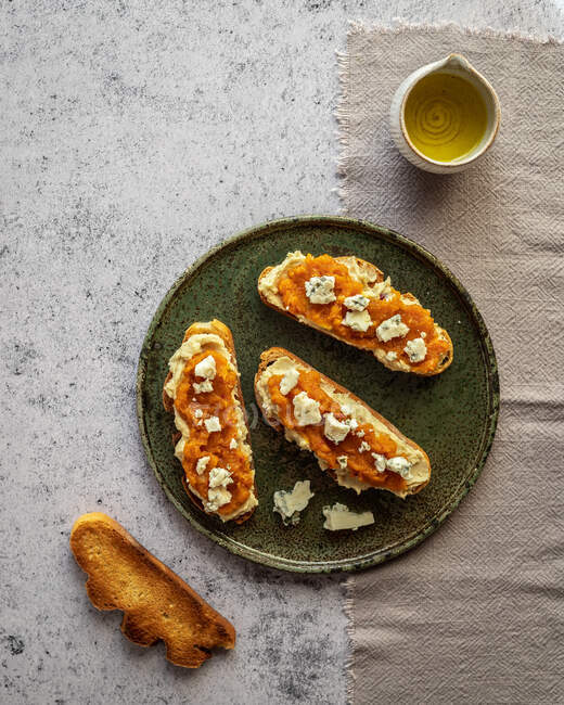 Vista dall'alto appetitosi toast freschi con marmellata e formaggio di capra serviti sul piatto vicino alla brocca con olio d'oliva biologico — Foto stock