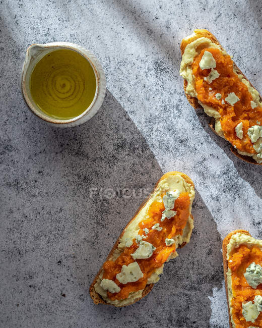 Overhead arrangement of wholesome pumpkin loaf toasts with sweet jam and goat cheese placed on marble table near pitcher of olive oil — Stock Photo