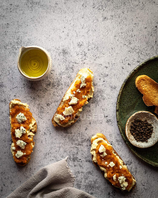 Overhead-Anordnung von gesunden Kürbisbrot Toasts mit süßer Marmelade und Ziegenkäse auf Marmortisch in der Nähe Krug mit Olivenöl platziert — Stockfoto